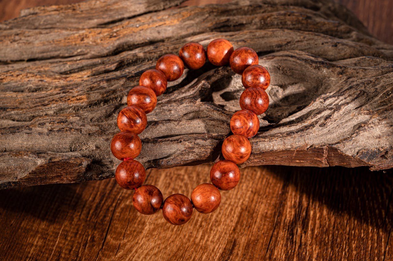 A close-up of a wooden beaded bracelet placed on textured driftwood, featuring warm tones.