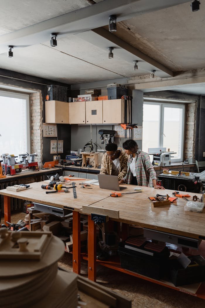 A diverse team collaborates on woodworking projects in a well-equipped workshop, using tools and a laptop for planning and execution.