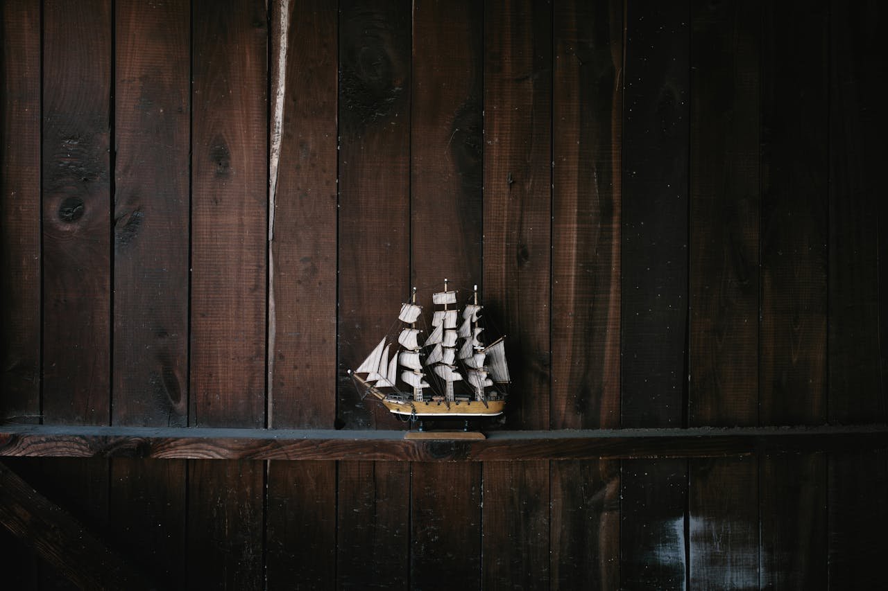 A detailed model ship displayed against a rich, dark wooden wall, evoking a sense of nautical history.