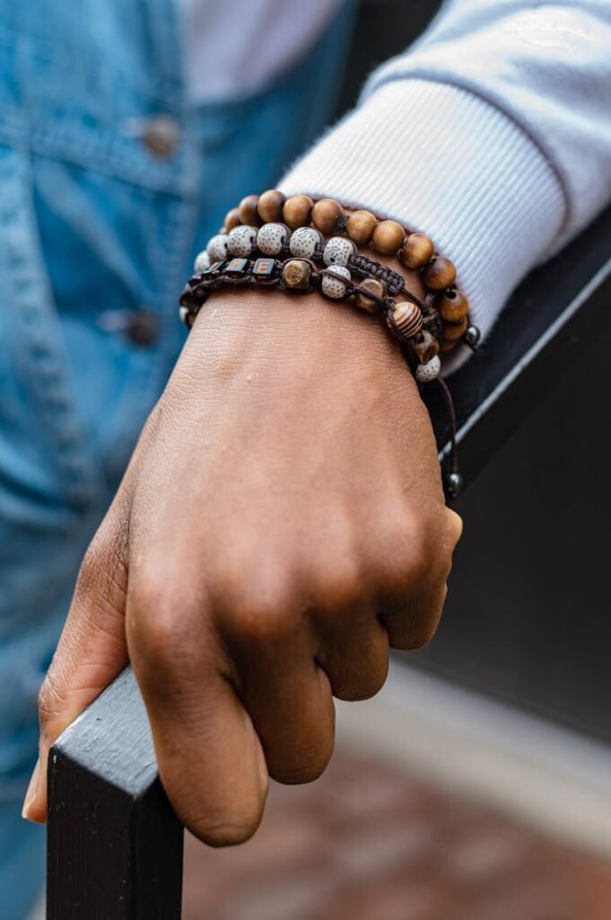 Hand holding railing adorned with multiple beaded bracelets in a casual setting.